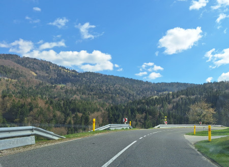 cesta, ki ima varnostno ograjo in prometno opremo za motoriste, v ozadju je pogled na hribe