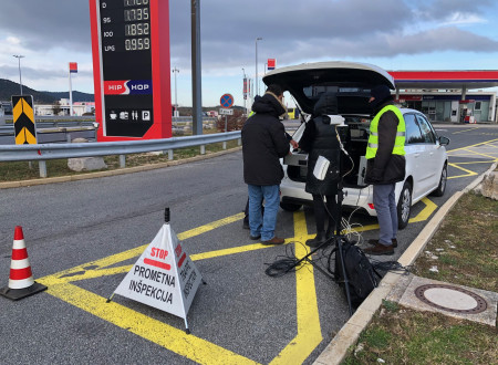 Na bencinskem servisu je vozilo, v katerem je antena DSRC in inšpektor za cestni promet predstavlja njeno delovanje