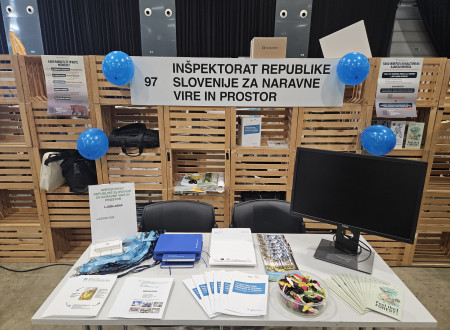 Razstavni prostor z napisom, na mizi promocijski material in letaki.