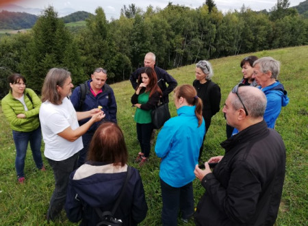 Udeleženci delavnice, oblečeni za hladnejše, vlažne, jesenske dni poslušajo mladega moškega, ki v rokah drži rumen cvet.