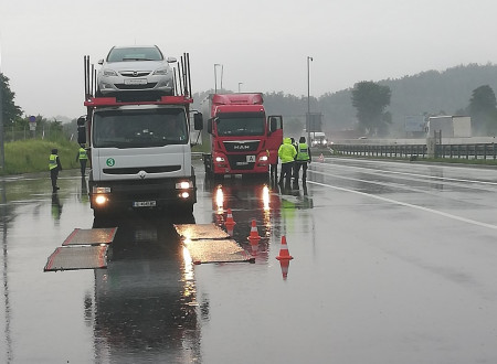 na parkirišču ob avtocesti stojita dva tovornjaka, ob obeh stojijo predstavniki finančne uprave in Inšpektorata za okolje in prostor v rumenih jopičih, ki preverjajo njihov tovor in dokumentacijo potrebno za prevoz odpadkov