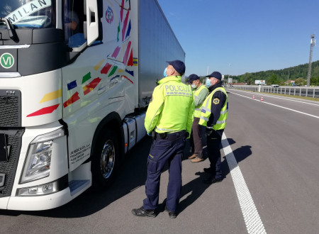 na levi strani je v ospredju desna stran kabine tovornega vozila ob kateri stojijo inšpektorji za okolje Inšpektorata za okolje in prostor, predstavniki Policije in Finančne uprave. Levo je cestišče in nad njim, v ozadju majhen hrib 