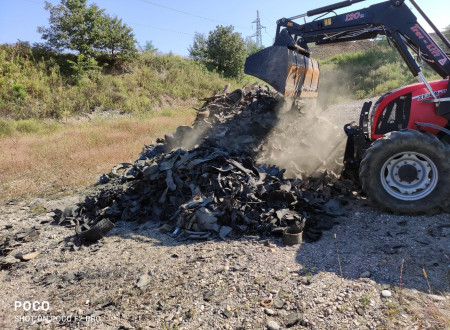 Udeleženci z lopatami grabljami in traktor, ki odvaža kupe preostanka gum.