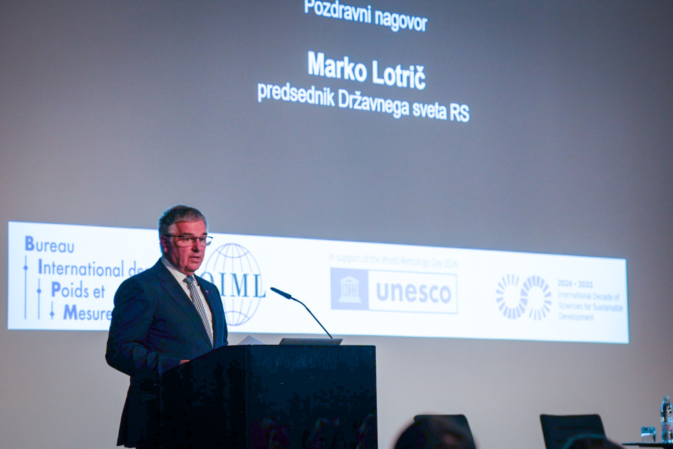 Moški govori za govorniškim pultom ob projekciji predstavitve na konferenci.