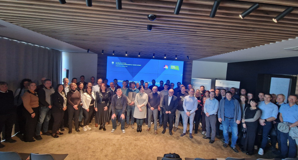 Na pročelju v dvorani je postavljenih približno 90 udeležencev dogodka.