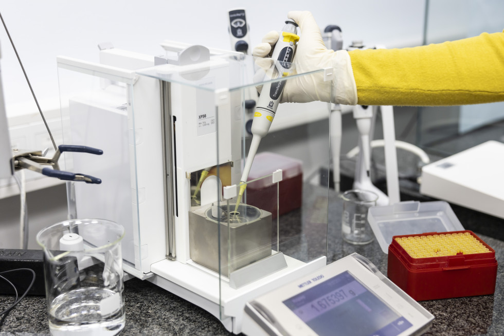 Na sliki je tehtnica in roka laboranta, ki na tehtnico s pipeto nanaša vzorec.