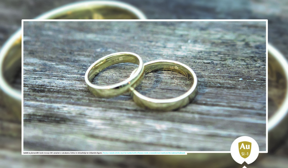 Na leseni podlagi sta dva zlata poročna prstana z vidnimi tremi oznakami.