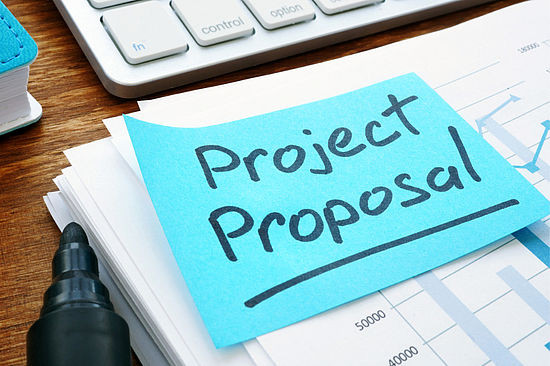 Miza s tipkovnico na katero je nalepljen modri listek z napisom (v angleščini) Project  Proposal 