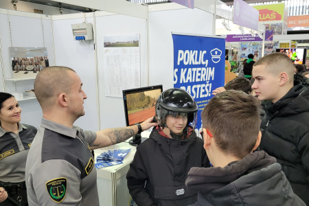 Obiskovalci na razstavnem prostoru uprave preizkušajo zaščitno opremo