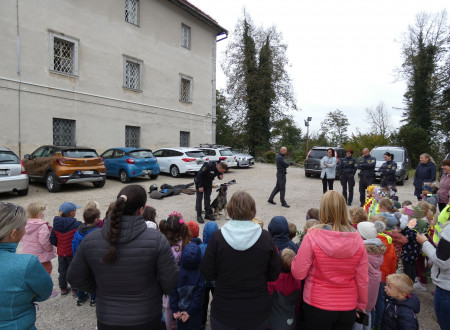 Obisk otrok iz vrtca na zunanjem dvorišču ženskega zapora, v sredini pravosodni policist in službeni pes