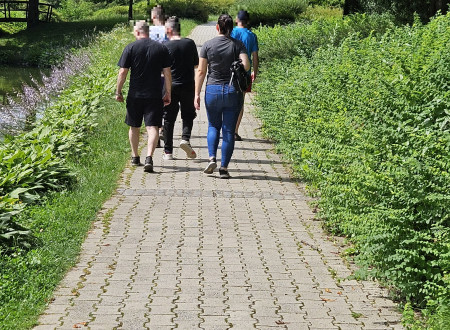 Skupina obsojencev in strokovna delavka, slikani v hrbet, na pohodu v mariborskem mestnem parku