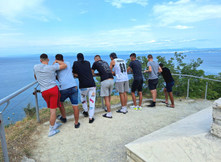 Mladoletniki s hrbtom obrnjeni slonijo na ograji, pod njimi je morski zaliv