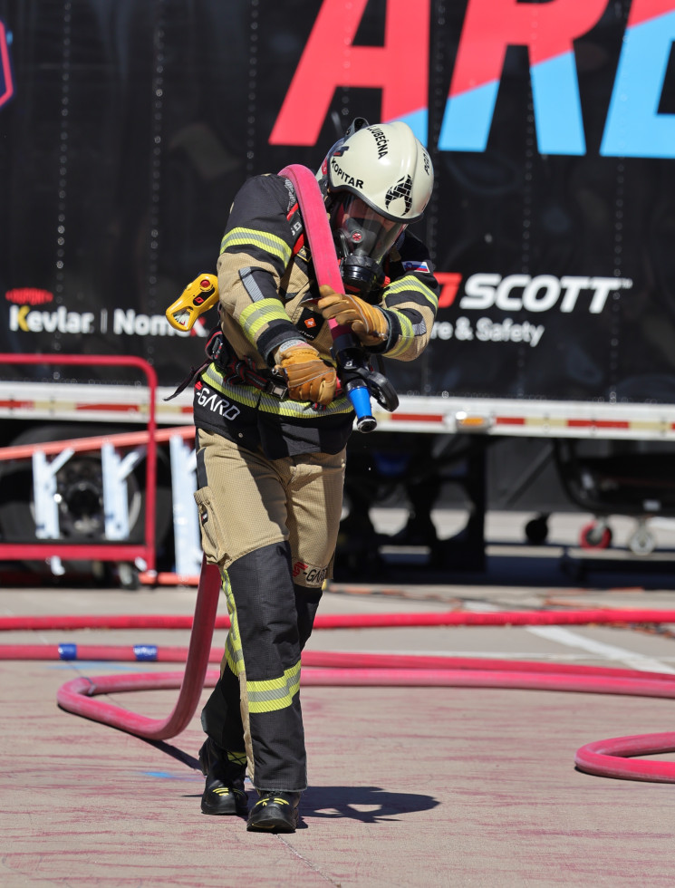Gasilec v polni opremi in na tekmovanju vleče 20 m gasilske cevi