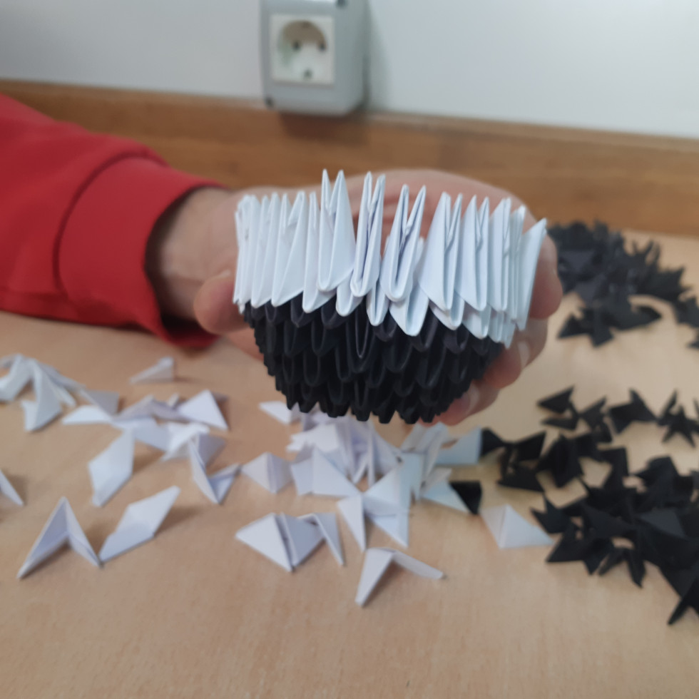 Začetna faza izdelave 3D origami pande: udeleženi sestavljajo prve papirnate module, pri čemer ponavljajoče prepogibanje krepi osredotočenost, mirnost in natančnost.