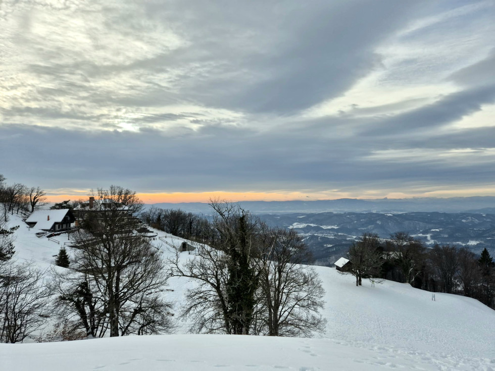 Zasneženi vrh Lisce in razgled v daljavo z nekaj oblakov in sončne svetlobe v ozadju.
