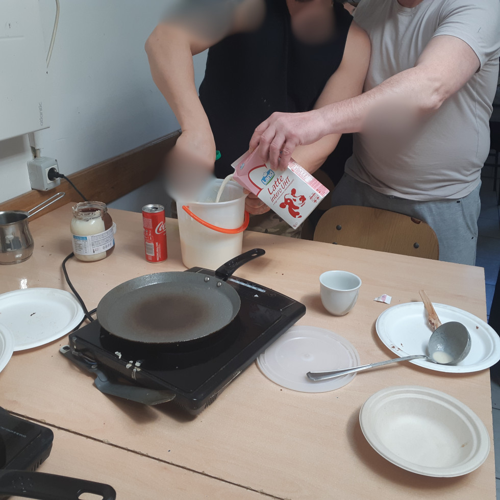 Dve osebi pripravljata maso za palačinke. Ena dodaja mleko, druga meša. Predstavljena je povezanost in sodelovanje.