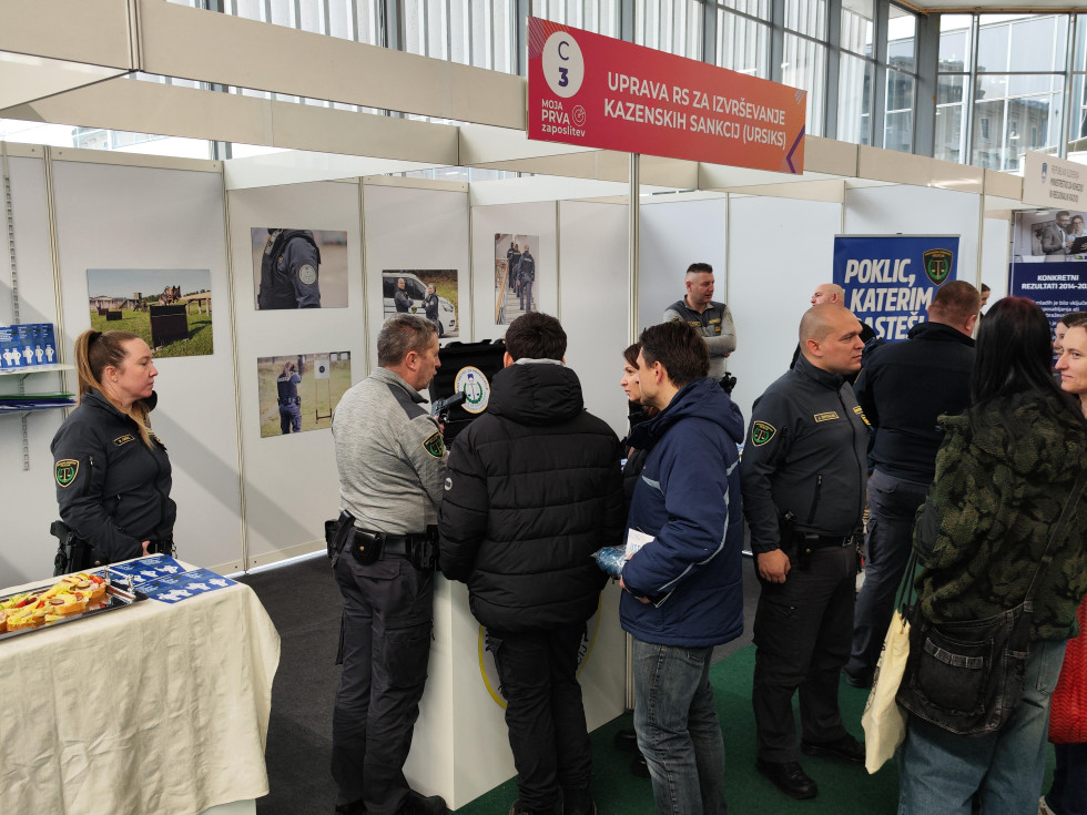 Več pravosodnih policistov, ki ob stojnici obiskovalcem razlagajo o poklicih v zaporskem sistemu.
