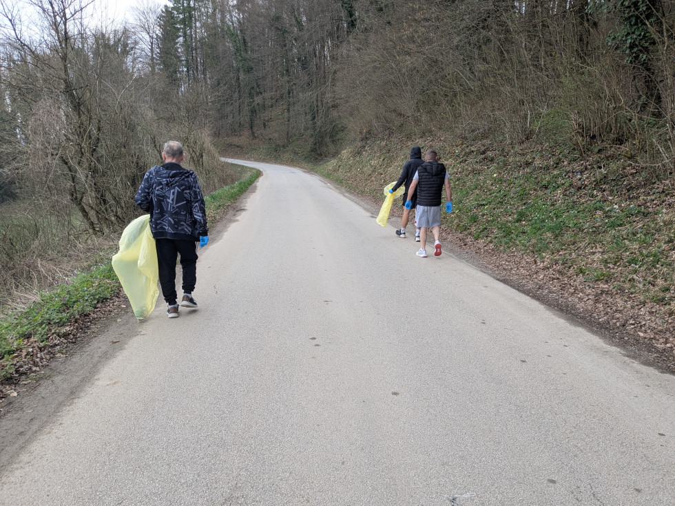 Trije moški ob robu ceste pobirajo smeti v vreče.