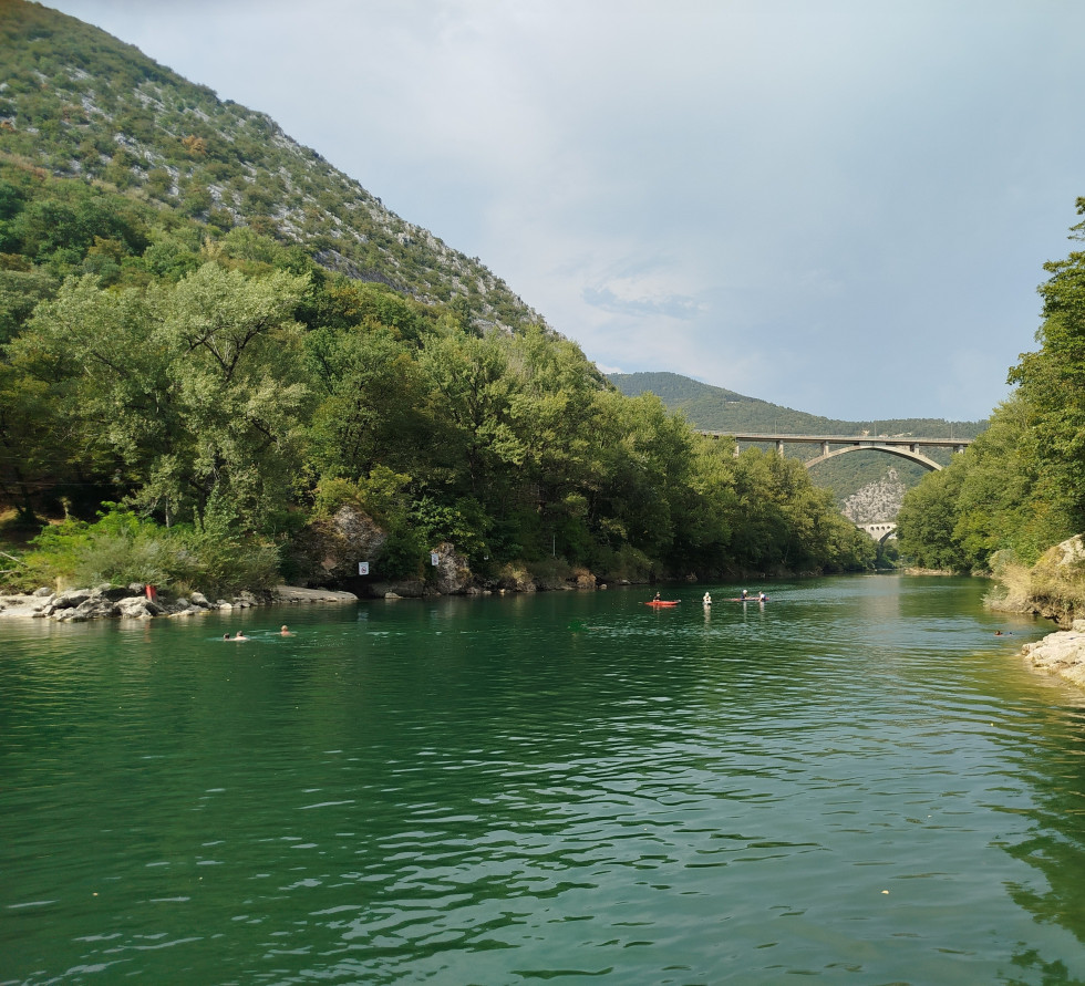Reka soča, ki je osvežila  obiskovalce, v ozadju je Solkanski most, na reki je tudi vdnih nekaj kajakašev.