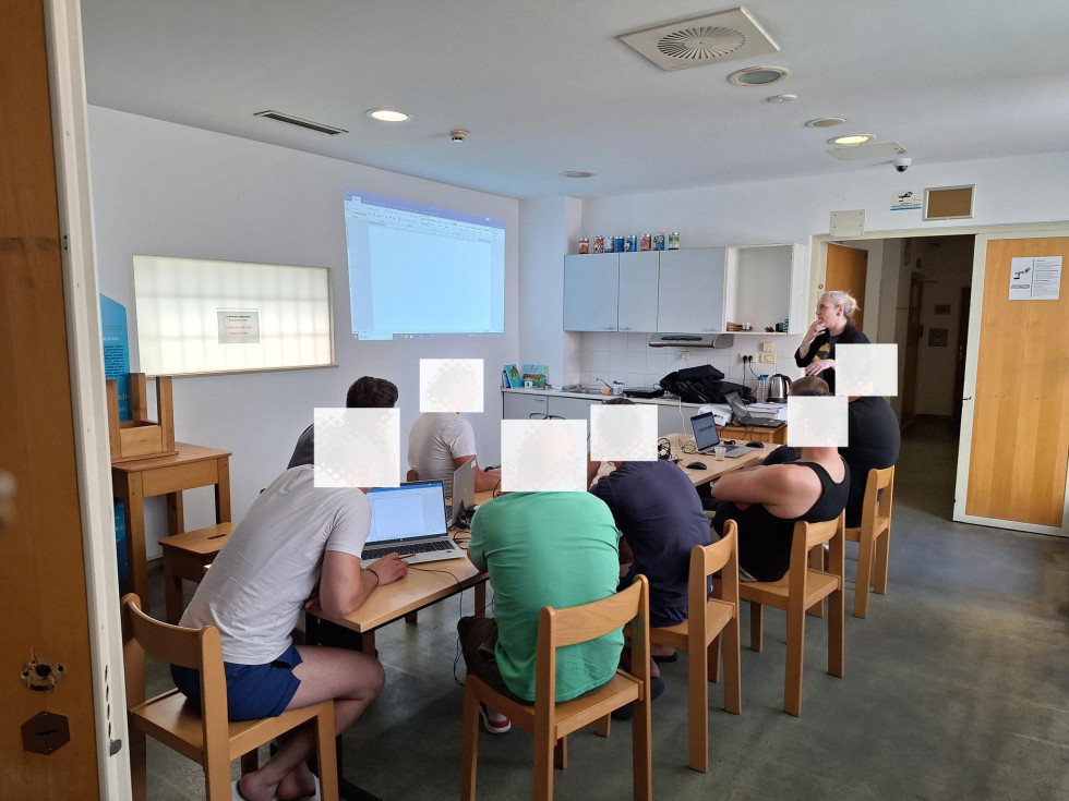 Sedem udeležencev sedi za mizo in spremlja predstavitev.