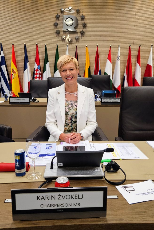 nasmejana karin žvokelj za mizo, pred njo napis karin žvokelj, chair mb, v ozadju na steni znak euipo in zastave držav članic