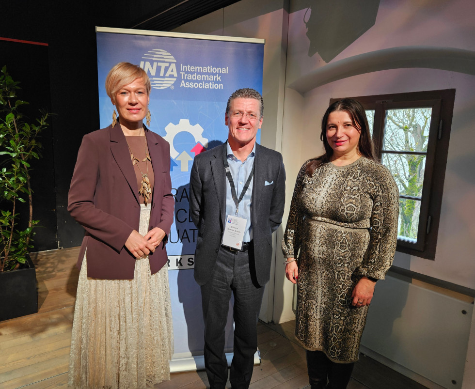 Mag. Karin Žvokelj, Etienne Sanz de Acedo in Ljuljana Kuterovac pozirajo za skupno fotografijo, v ozadju pano z logotipom INTA