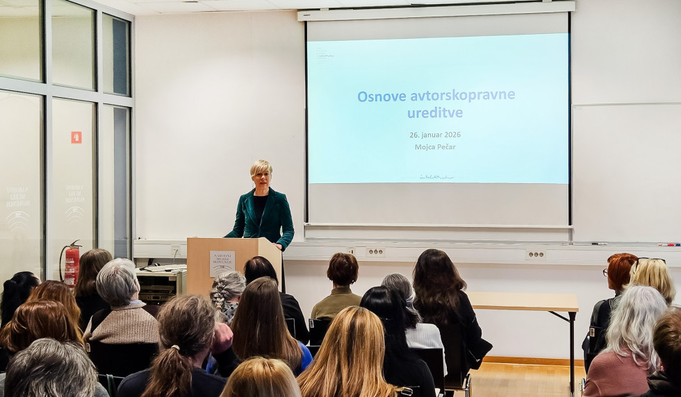 Mag. Karin Žvokelj med nagovorom pred vrstami udeležencev, v ozadju projekcija z naslovom delavnice