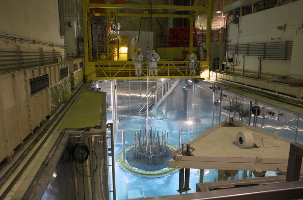 Nad odprtim prostorom za jedrsko gorivo so osvetljene gorivne palice, na ploščadi nad njimi trije delavci v zaščitnih oblačilih.