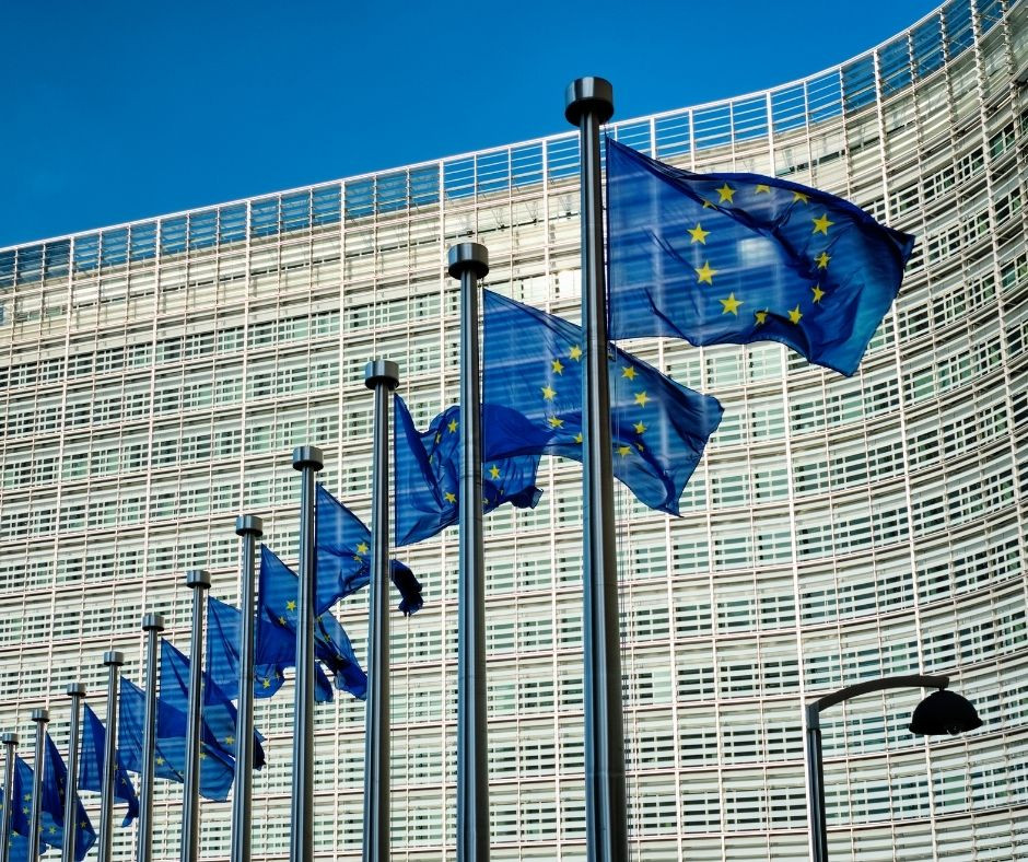 Zastave EU na drogovih. Plapolajo v vetru. V ozadju stavba in modro nebo.
