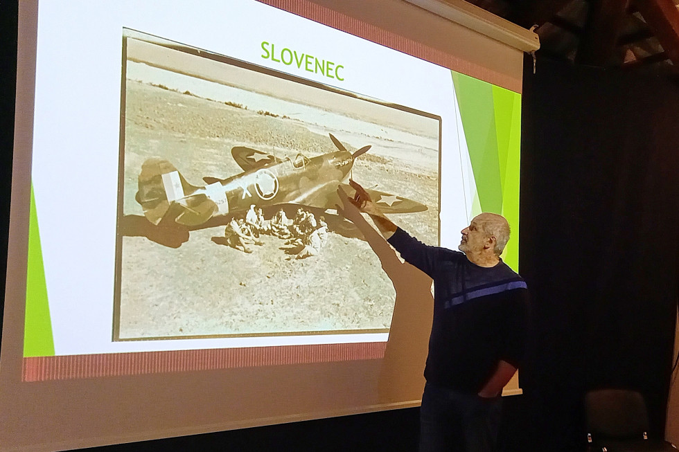Aleš Bedič stoji in kaže na sliko letala Spitfire Slovenec.