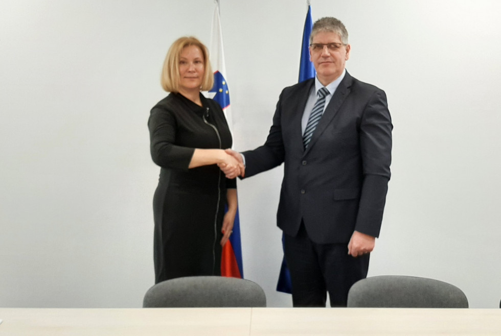 Direktor in gostja se rokujeta. Za njima sta zastavi Slovenije in EU