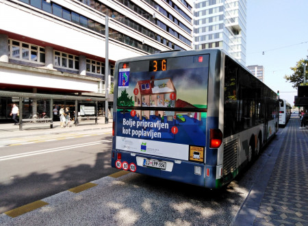 Na fotografiji je vidna zadnja stran zgibnega avtobusa, ki stoji na avtobusni postaji. Na avtobusu je ilustracija hiše in garaže, ki sta delno poplavljeni. Viden je bel napis Bolje pripravljen kot poplavljen in logotip Evropske Unije, Kohezijski sklad.