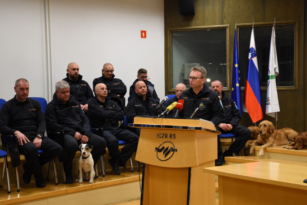 Direktor za govorniškim pultom v ozadju sedijo pripadniki z reševalnimi psi.