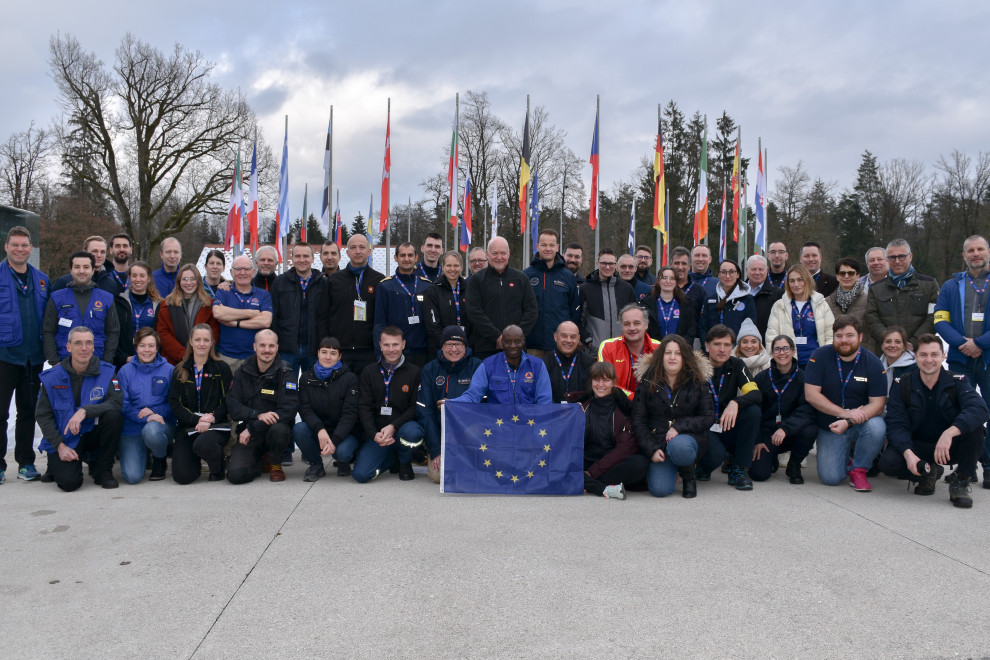 Vsi udeleženci v ospredju, v sredini oseba drži zastavo Evropske unije, v ozadju je krog zastav držav Evropske unije.