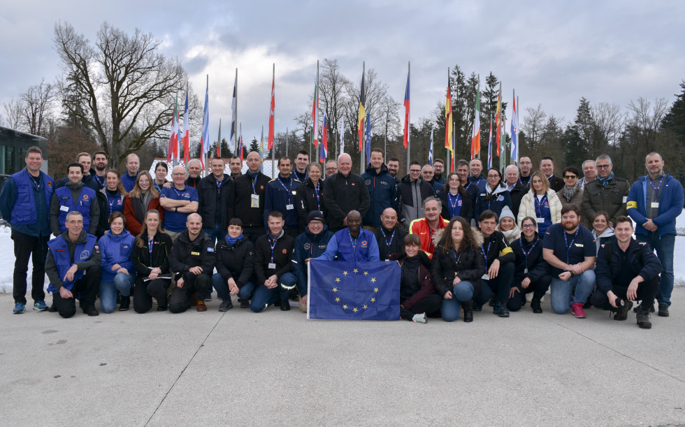 Vsi udeleženci v ospredju, v sredini oseba drži zastavo Evropske unije, v ozadju je krog zastav držav Evropske unije.