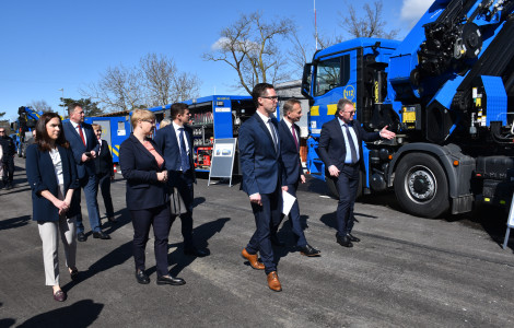 Predstavitev posebne opreme. (People walking past trucks in blue color.)