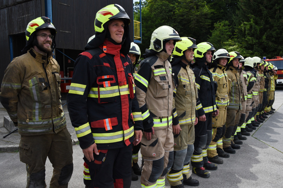 Gasilci z nasmejanimi obrazi in v uniformah postavljeni v dveh vrstah.