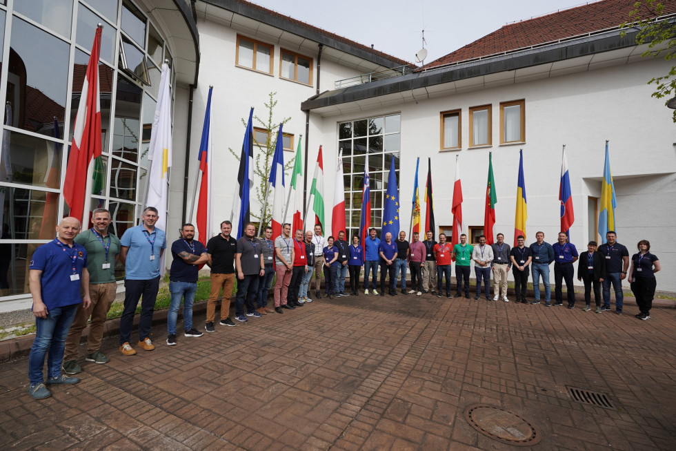 Udeleženci stojijo pred zastavami vseh držav iz katerih prihajajo. V ozadju izobraževalni center.