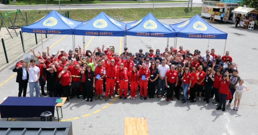 skupinska slika udeležencev prireditve, ki stojijo pod štirimi modrimi nadstreški