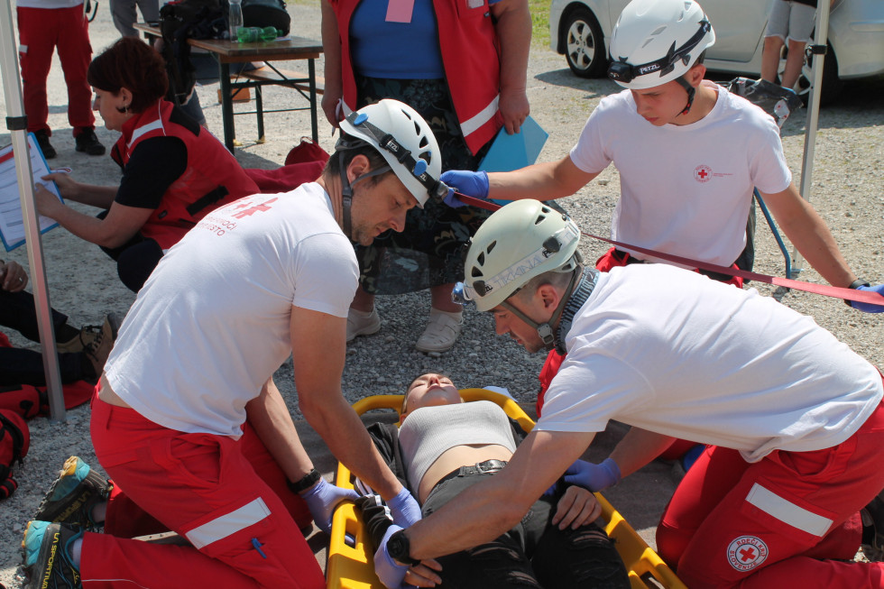 Trije pripadniki Rdečega križa Slovenija med izvajanjem prve pomoči osebi na nosilih.