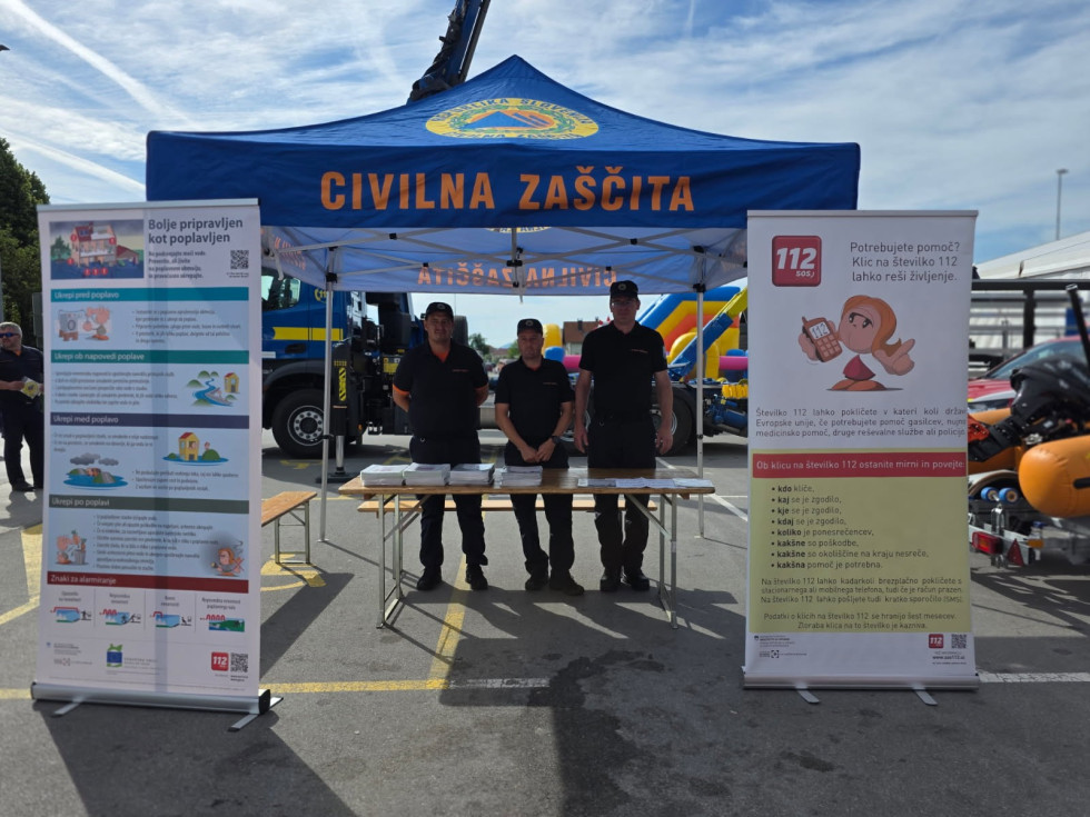 Predstavniki sodelujočih institucij stojijo med predstavitvenimi panoji na dogodku s področja civilne zaščite.
