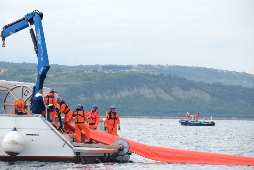 Na fotografiji je ladja, s katere razvijajo lovilce za oljni madež, v odzadju še en čloln