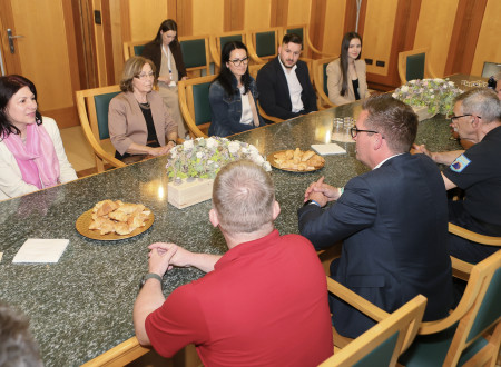 Na sliki je skupina ljudi, ki sedi za mizo. Med njimi so žena in dve hčerki nekdanjega poveljnika CZ Mirana Bogataja ter njegova vnuka, župan Nove Gorice in Leon Behin, generalni direktor URSZR