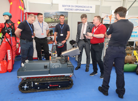 Na fotograiji je skupina ljudi, ki stoji pred robotom za odkrivanje bomb