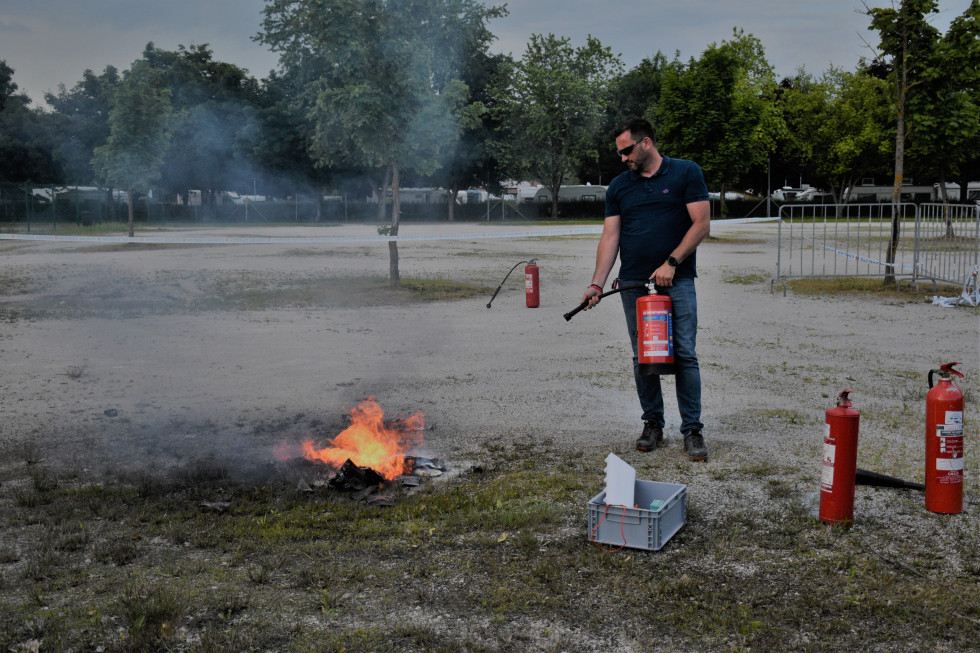 Na parkirišču plamen, kjer gori baterija, moški gasi z gasilnim aparatom.