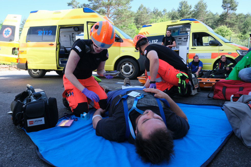 Dva reševalca nudita prvo pomoč ponesrečencu v ozadju dva reševalna vozila.