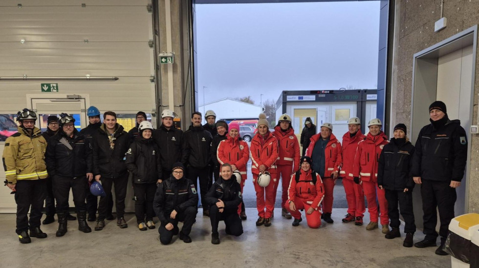 Skupinska fotografija v skladišču, udeleženci so oblčeni v uniforme modre in rdeče barve.