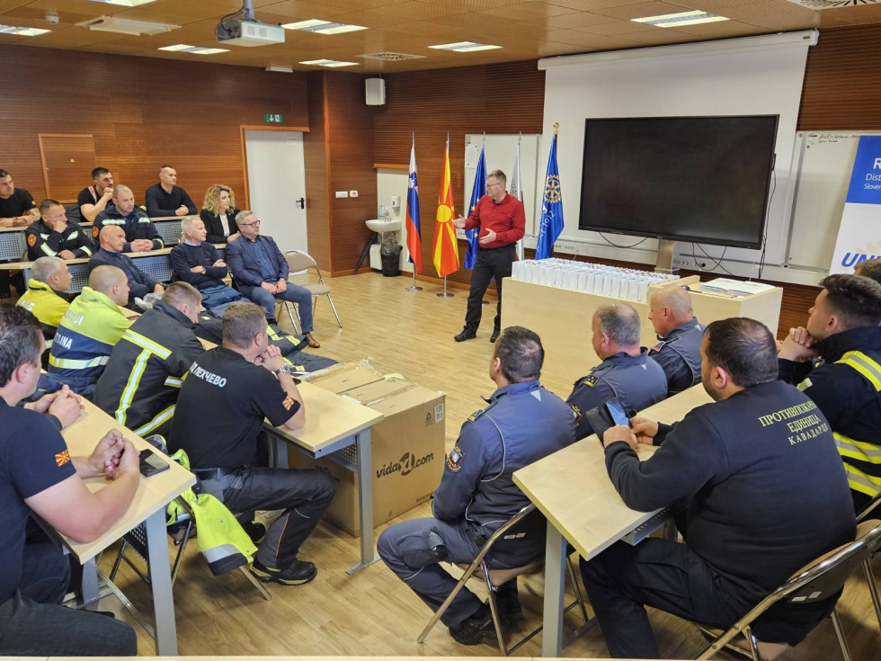 Slika prikazuje udeležence tečaja, ki so postrojeni in v vrsti, pred njimi je zaščtina gasilska oprema, ki jo je SLovenija donirala Severni Makedoniji.
