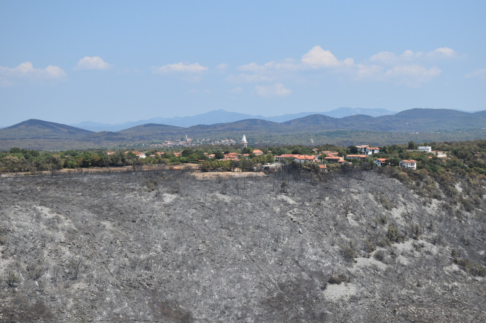 Požgan vrh do platoja na njem pa cerkev. V ozadju so videni hribi.