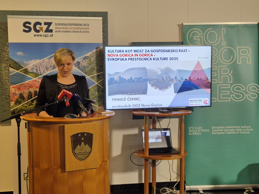 Maja Balant Slobodjanac stoji za govorniškim pultom in govori. Zadaj ekran z predstavitvijo